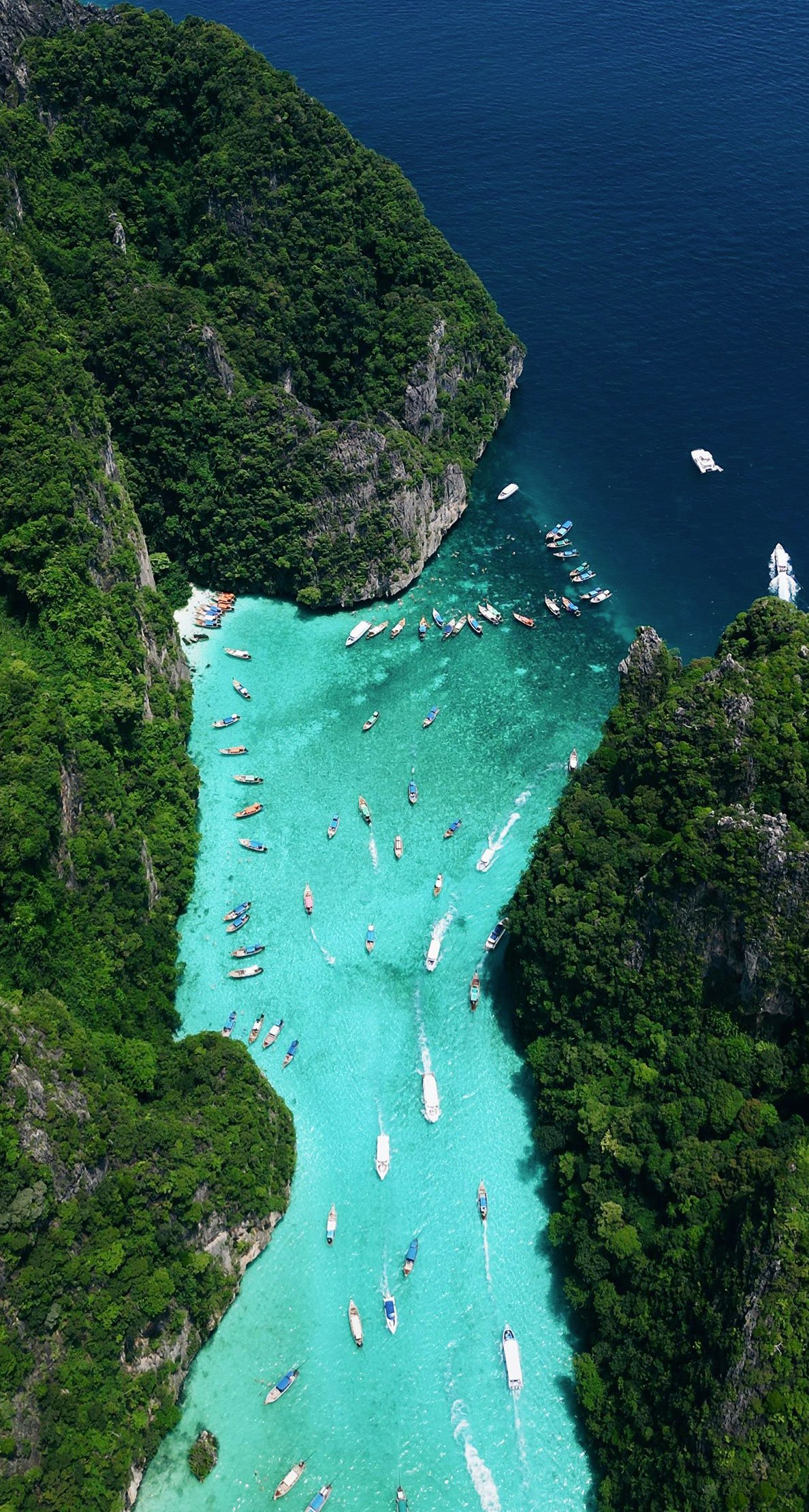 Aerial view of boats floating in the turquoise waters of a bay enclosed by cliffs in Thailand