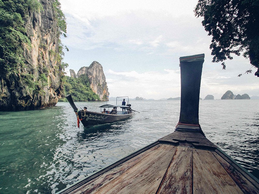Prow of a traditional wooden Thai long-tail boat sailing on turquoise water